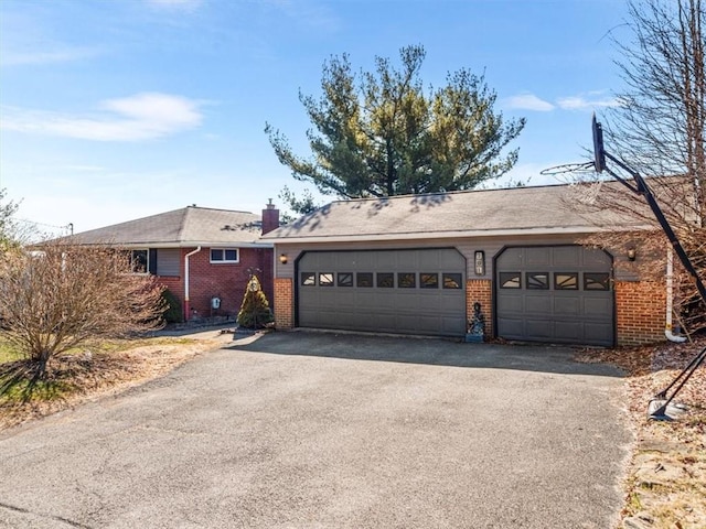 single story home with an attached garage, a chimney, aphalt driveway, and brick siding