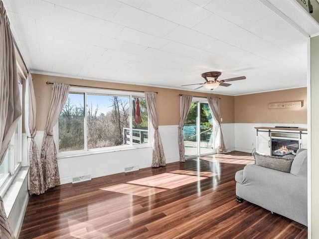 unfurnished living room featuring wood finished floors, wainscoting, a glass covered fireplace, and visible vents