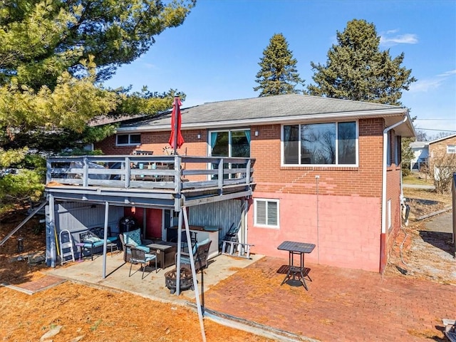 rear view of property featuring a fire pit, a patio, brick siding, and a wooden deck