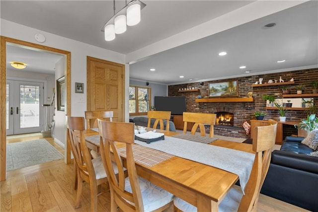 dining room with a fireplace, recessed lighting, light wood-style floors, and brick wall