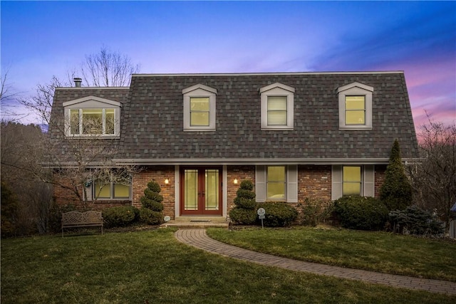 view of front of house with a front yard, french doors, brick siding, and a shingled roof