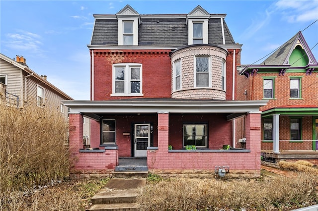 victorian home with brick siding, covered porch, mansard roof, and roof with shingles