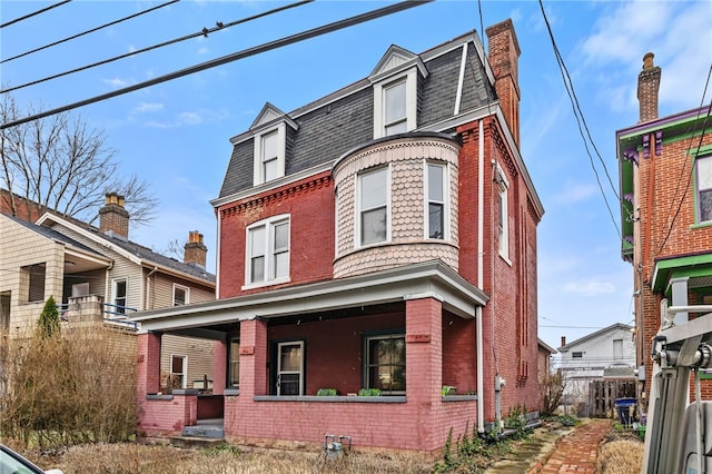 view of front of home featuring mansard roof, a porch, fence, a shingled roof, and brick siding