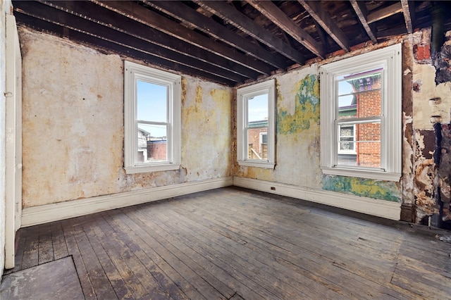 empty room featuring a healthy amount of sunlight, baseboards, and wood-type flooring