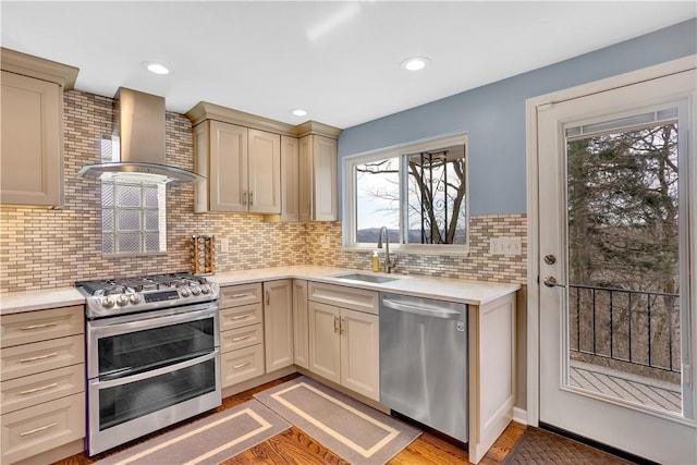 kitchen featuring light countertops, light wood-style flooring, appliances with stainless steel finishes, a sink, and wall chimney exhaust hood