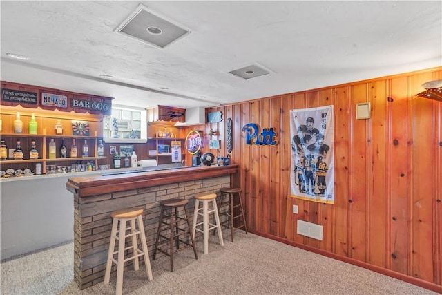 bar with a bar, wood walls, carpet, and visible vents