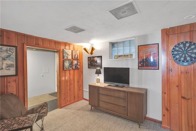 living area featuring light colored carpet, wood walls, and baseboards