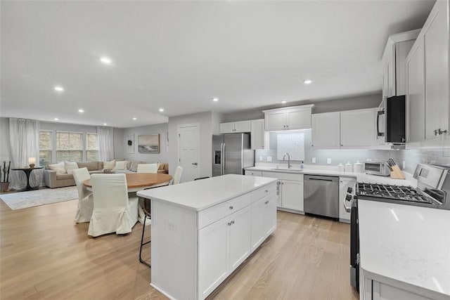 kitchen featuring a center island, stainless steel appliances, light wood-type flooring, white cabinetry, and a sink