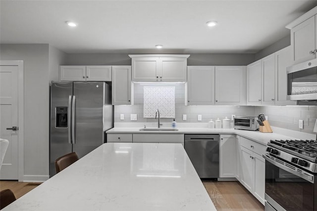 kitchen with appliances with stainless steel finishes, decorative backsplash, a sink, and light wood-style floors