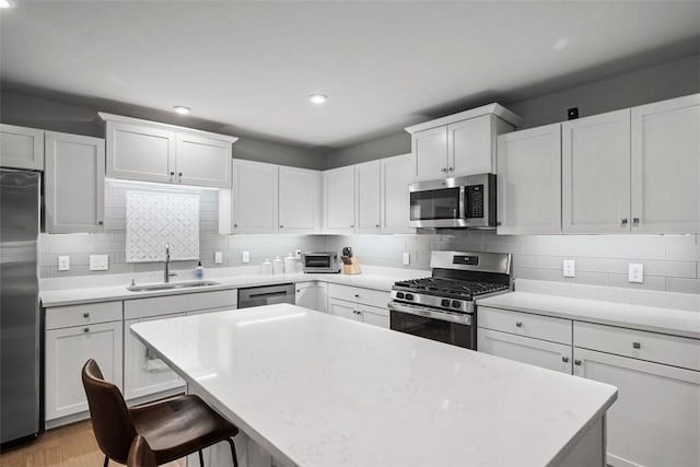 kitchen featuring a sink, light countertops, appliances with stainless steel finishes, a center island, and tasteful backsplash