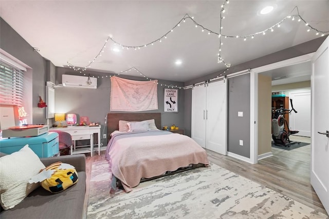 bedroom with a barn door, baseboards, wood finished floors, and a wall mounted air conditioner