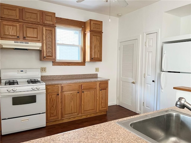 kitchen with under cabinet range hood, white appliances, dark wood-type flooring, a sink, and brown cabinetry