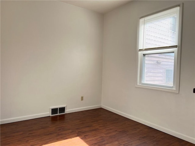 unfurnished room featuring dark wood-style floors, a wealth of natural light, visible vents, and baseboards