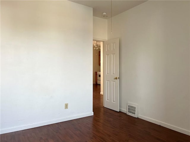 unfurnished room featuring dark wood-type flooring, visible vents, and baseboards