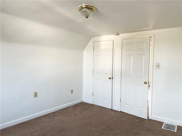 additional living space featuring lofted ceiling, dark carpet, visible vents, and baseboards