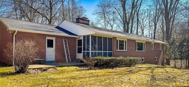 exterior space with a yard, a sunroom, a chimney, and brick siding