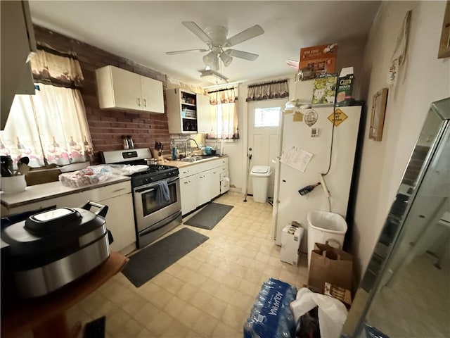 kitchen with stainless steel range with gas cooktop, light floors, a ceiling fan, white cabinetry, and a sink