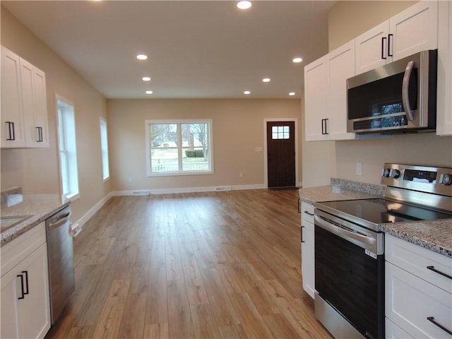 kitchen with open floor plan, stainless steel appliances, light wood finished floors, and white cabinetry