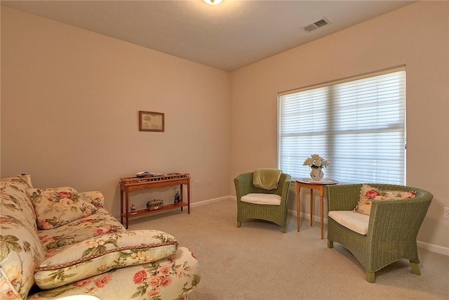 living area featuring baseboards, visible vents, and light colored carpet