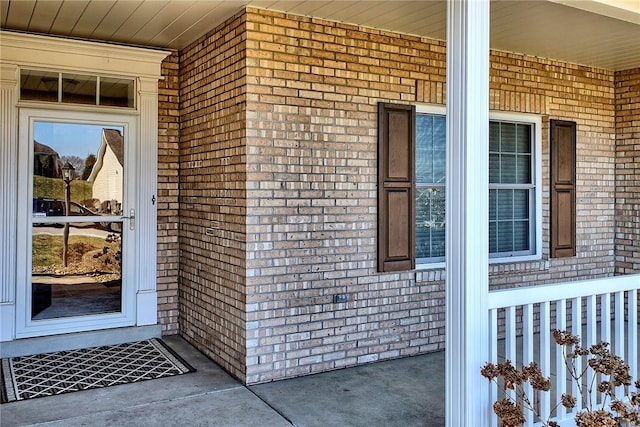 view of exterior entry featuring covered porch and brick siding