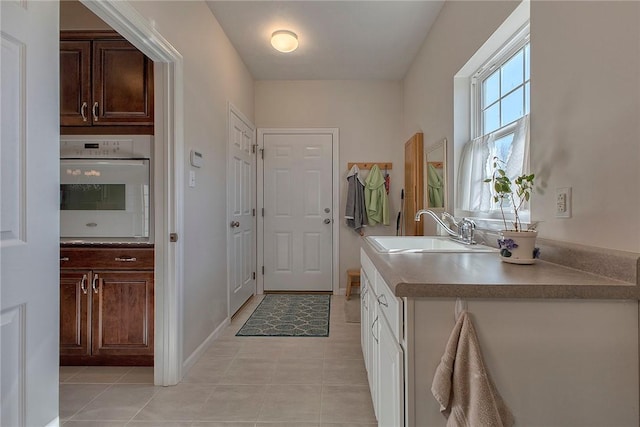 kitchen featuring white oven, light tile patterned floors, a sink, dark brown cabinets, and baseboards