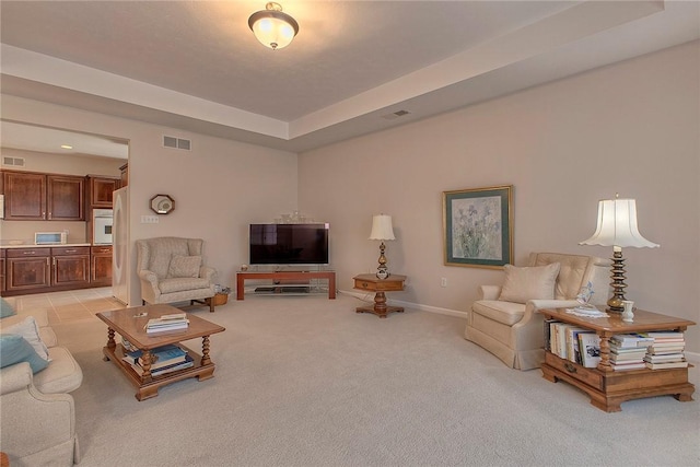 living room with baseboards, visible vents, a tray ceiling, and light colored carpet