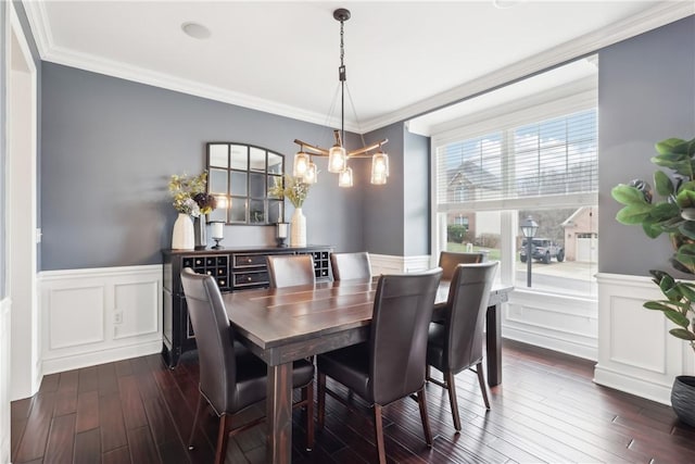 dining area featuring an inviting chandelier, crown molding, dark wood-style flooring, and wainscoting