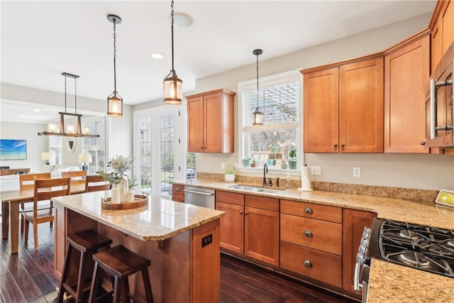 kitchen with light stone counters, dark wood-style flooring, a sink, appliances with stainless steel finishes, and a center island