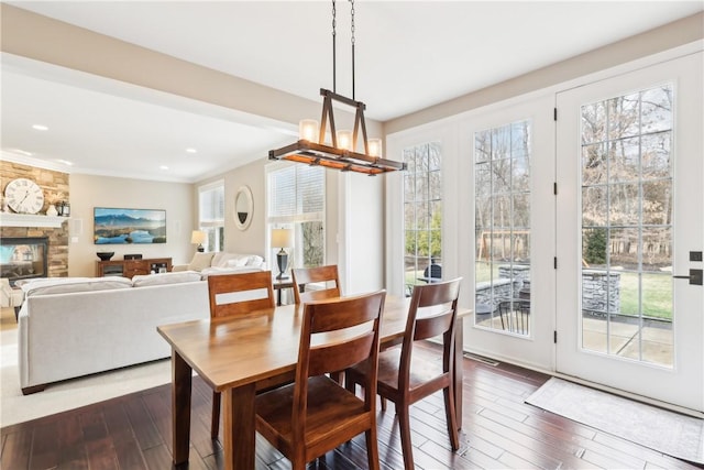 dining area featuring dark wood-style flooring, crown molding, a fireplace, a chandelier, and recessed lighting