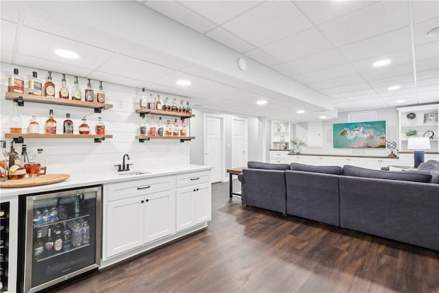 bar featuring wine cooler, a drop ceiling, a sink, wet bar, and dark wood finished floors