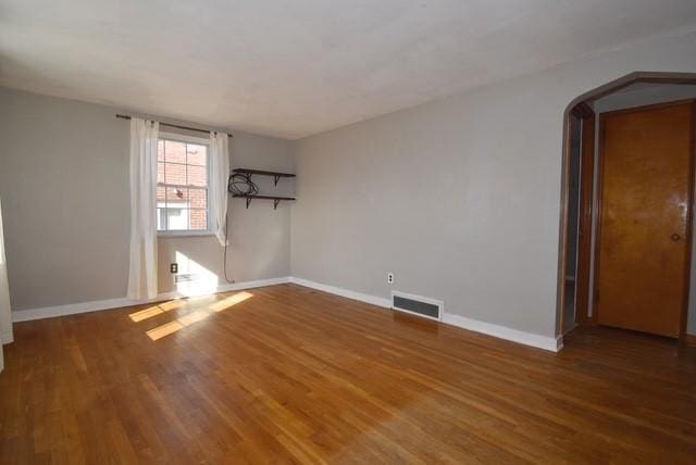 spare room featuring arched walkways, wood finished floors, visible vents, and baseboards