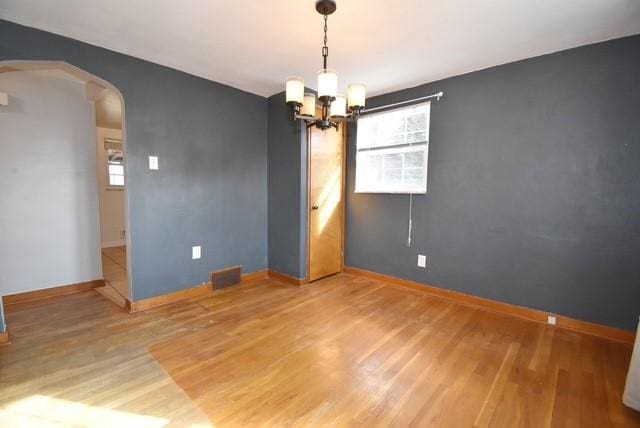 unfurnished room featuring arched walkways, a notable chandelier, wood finished floors, visible vents, and baseboards