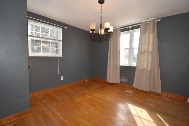 spare room featuring baseboards, wood finished floors, and an inviting chandelier