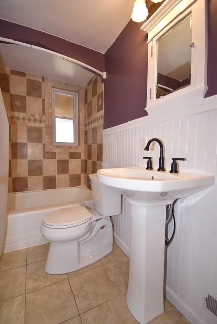 full bath featuring toilet, wainscoting, a sink, tub / shower combination, and tile patterned flooring