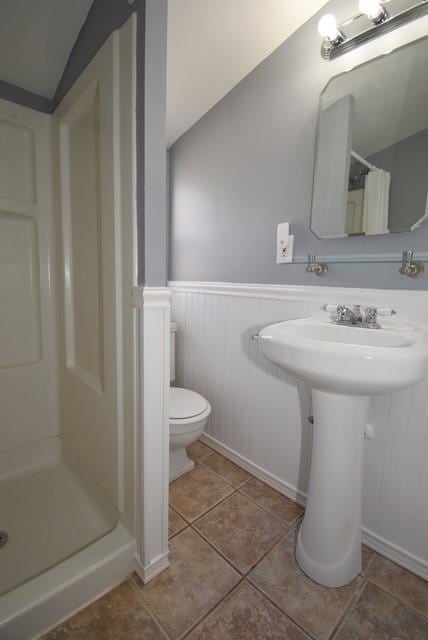 bathroom featuring a stall shower, wainscoting, tile patterned flooring, and toilet