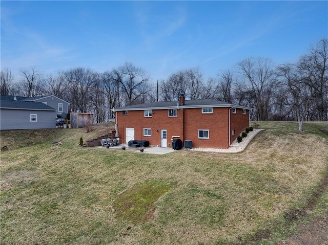 rear view of house with a lawn, a patio, a chimney, central air condition unit, and brick siding