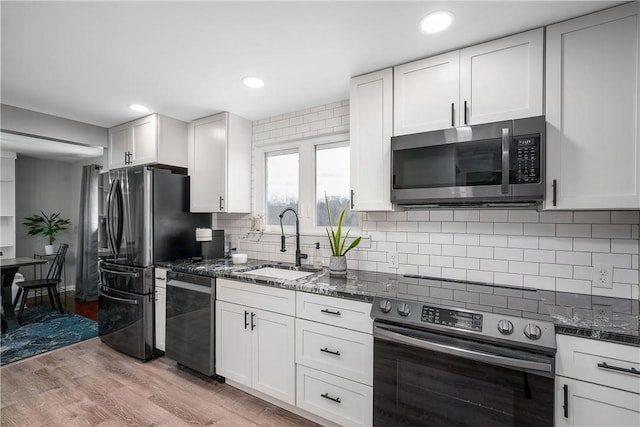 kitchen with light wood finished floors, white cabinets, dark stone counters, stainless steel appliances, and a sink