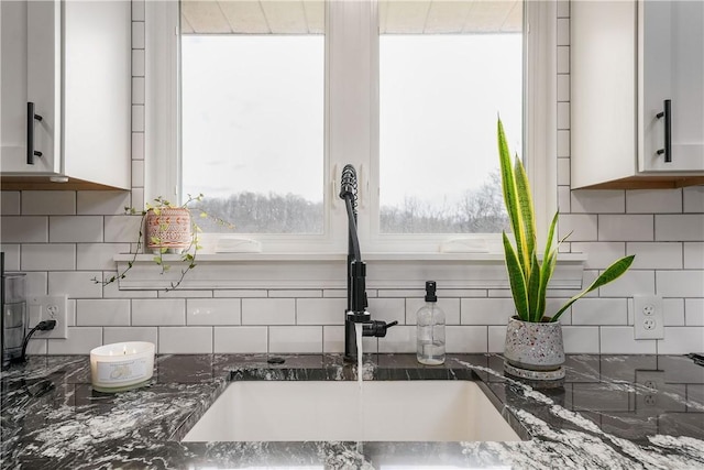 kitchen featuring dark stone counters, backsplash, a sink, and white cabinets