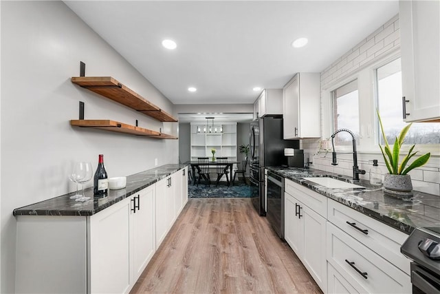 kitchen featuring black appliances, light wood finished floors, a sink, and white cabinetry