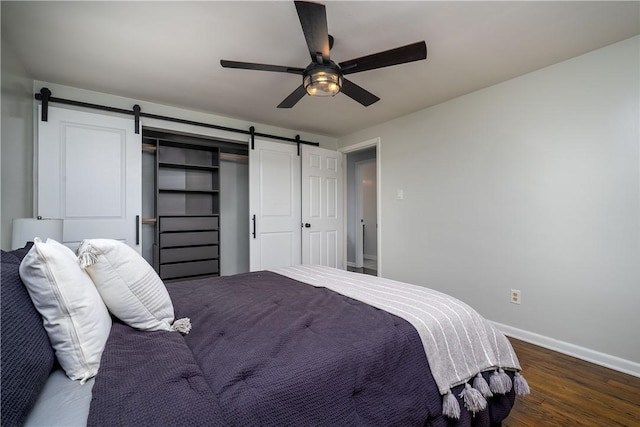 bedroom with wood finished floors, ceiling fan, baseboards, and a barn door