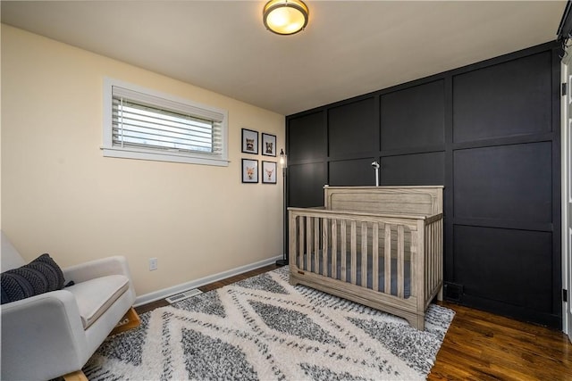 bedroom with dark wood-style flooring, visible vents, a decorative wall, and baseboards