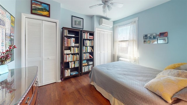 bedroom featuring a wall unit AC, multiple closets, radiator heating unit, ceiling fan, and wood finished floors