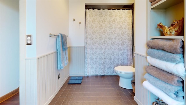 bathroom featuring curtained shower, wainscoting, tile patterned flooring, and toilet