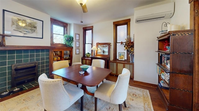 dining room with a tiled fireplace, baseboards, wood finished floors, and a wall mounted air conditioner