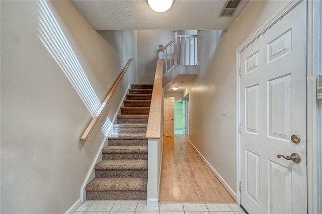 stairway featuring tile patterned flooring, visible vents, a textured ceiling, and baseboards