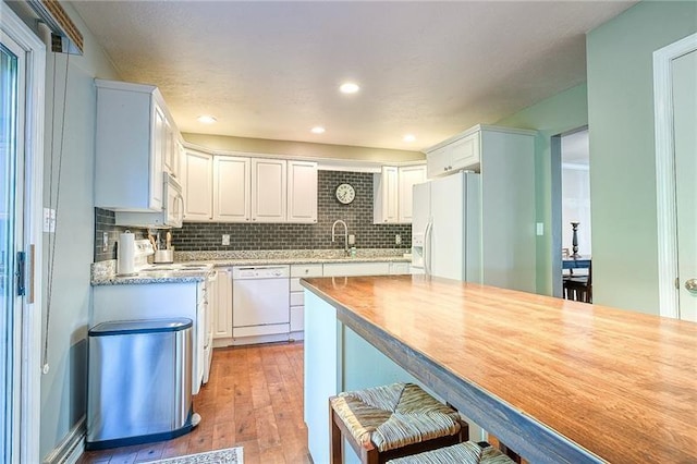 kitchen featuring light countertops, backsplash, white cabinets, a sink, and white appliances