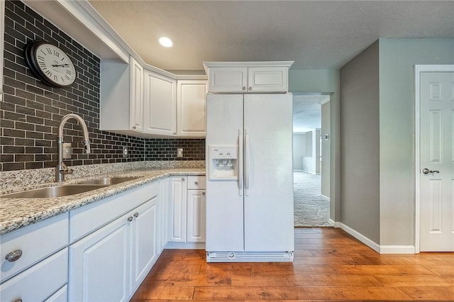 kitchen with tasteful backsplash, white fridge with ice dispenser, white cabinets, and a sink