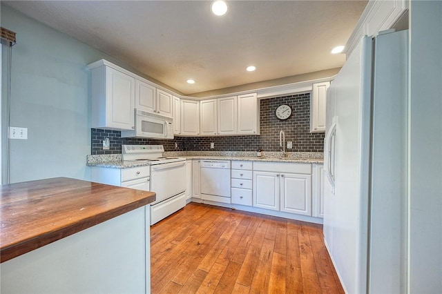 kitchen featuring white appliances, a sink, white cabinetry, light wood-type flooring, and decorative backsplash