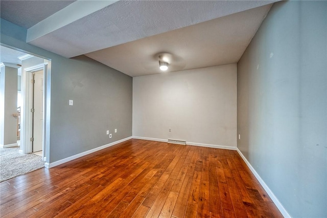 spare room featuring a baseboard heating unit, baseboards, and hardwood / wood-style floors