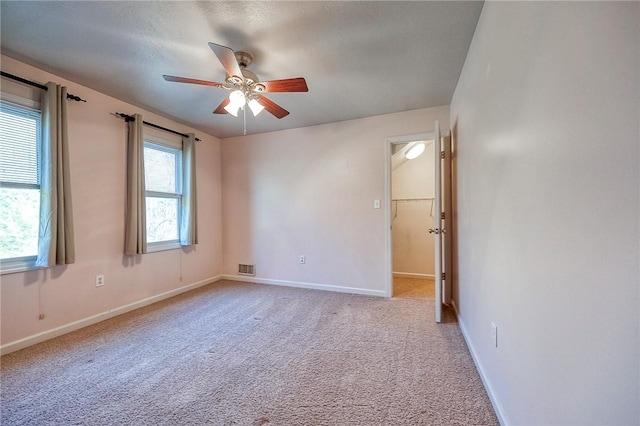 empty room featuring light carpet, a ceiling fan, visible vents, and baseboards